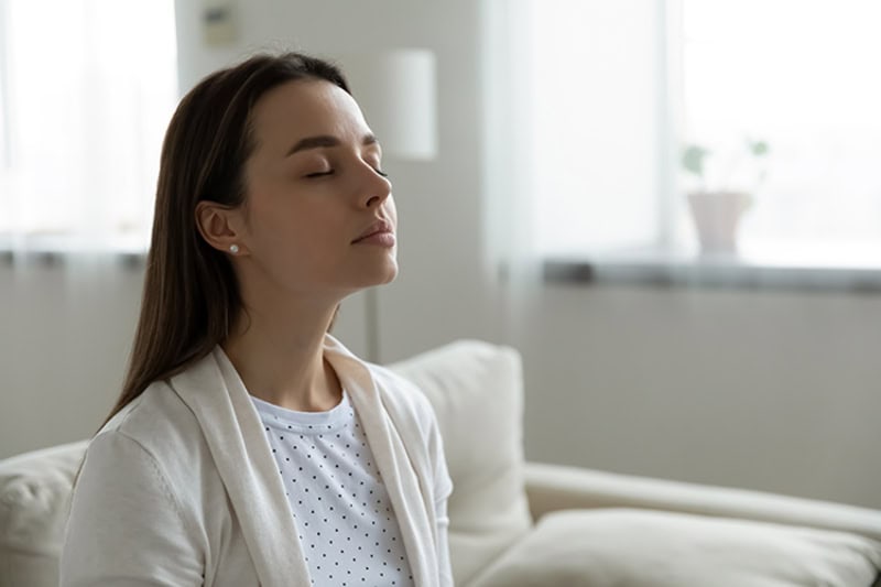woman sitting in her living room, taking a deep breath of clean air.
